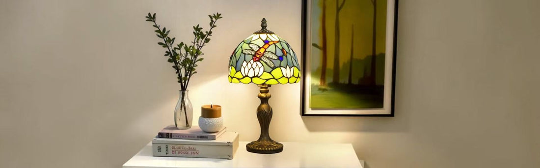 Tiffany dragonfly table lamp glowing green and amber on white console table with books and vase