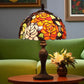 Stained glass lamp on a table with a green sofa and floral arrangement in the background. CDH Tiffany Table Lamp