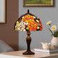Stained glass table lamp on a surface with a vase of flowers and books in the background. CDH Tiffany Table Lamp.