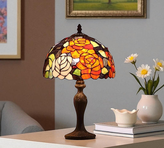 Stained glass table lamp on a surface with a vase of flowers and books in the background. CDH Tiffany Table Lamp.