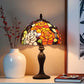Decorative table lamp with stained glass shade on a shelf next to a white vase and books. CDH Tiffany Table Lamp