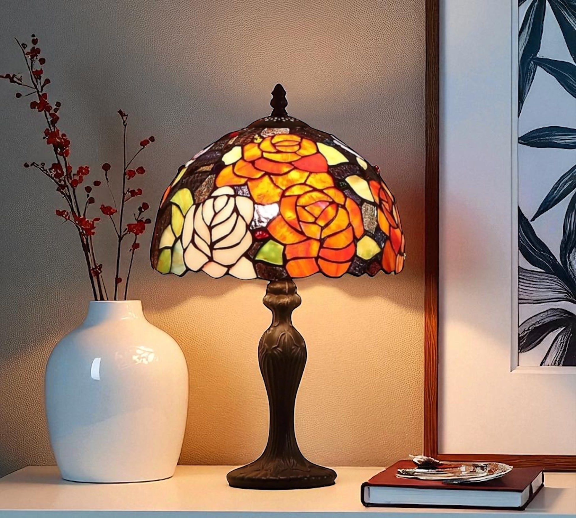 Decorative table lamp with stained glass shade on a shelf next to a white vase and books. CDH Tiffany Table Lamp