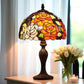 Stained glass table lamp with a colorful design on a table next to a vase of white tulips. CDH Tiffany Table Lamp.