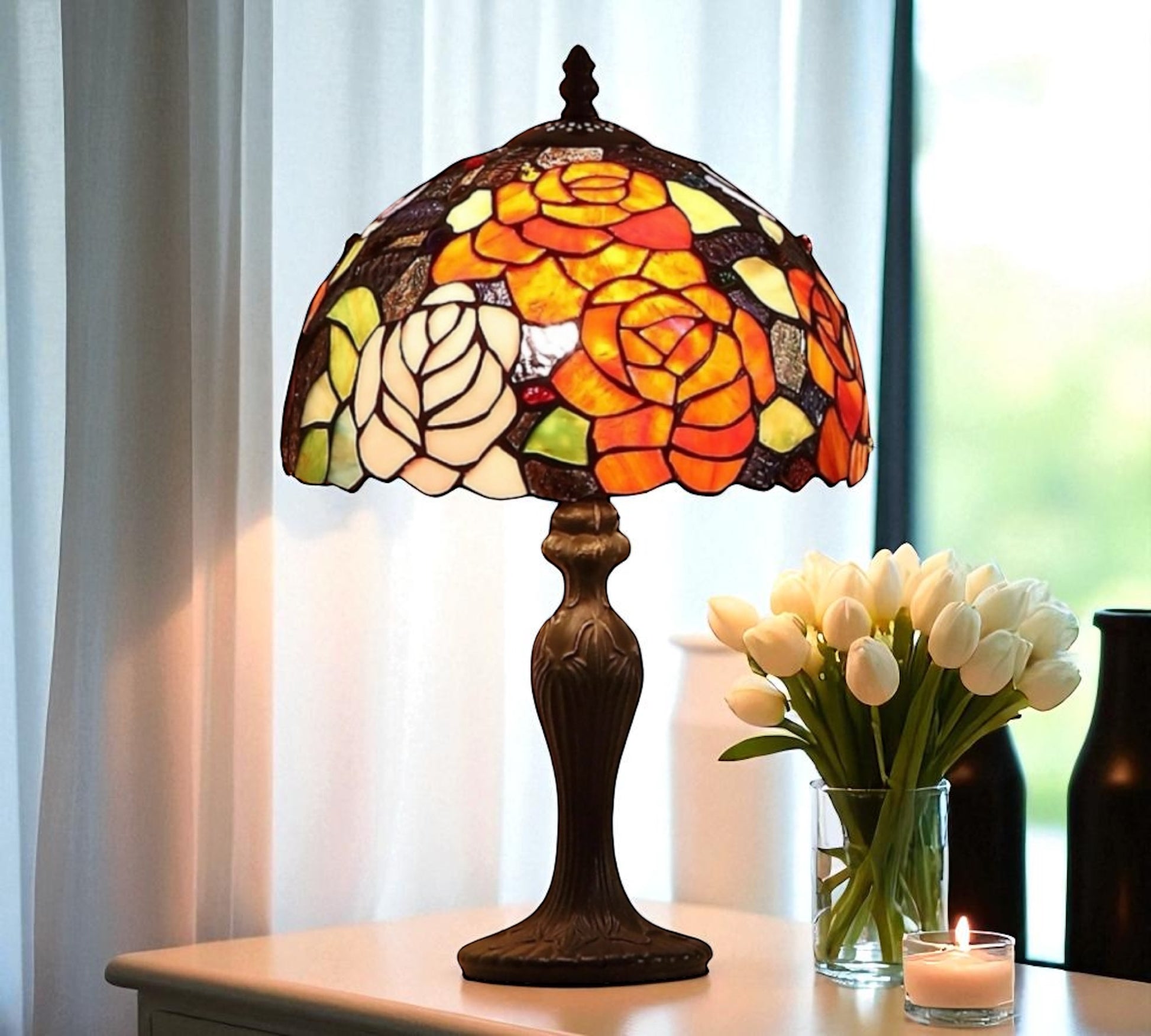 Stained glass table lamp with a colorful design on a table next to a vase of white tulips. CDH Tiffany Table Lamp.