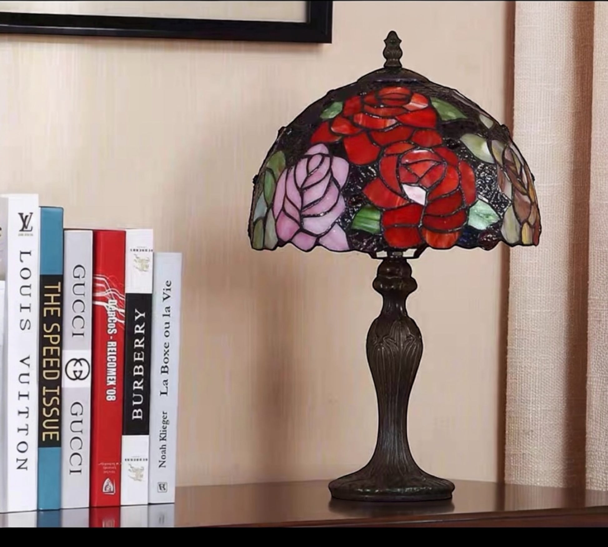 Decorative table lamp with stained glass shade featuring roses on a shelf with books. CDH Tiffany Table Lamp