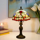 Tiffany-style stained glass table lamp with red floral shade and bronze base on tabletop.
