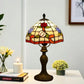 Tiffany-style stained glass table lamp with red floral shade and bronze base on side table.