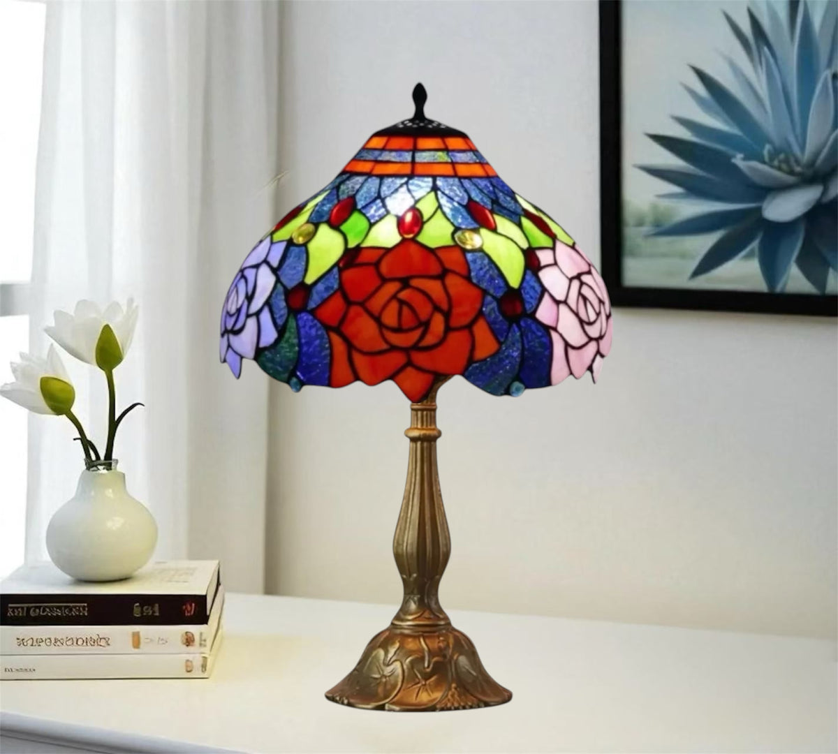 Stained glass table lamp with red rose shade and bronze base on a tabletop.