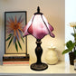 Tiffany table lamp with pink stained-glass shade, ornate dark base, bulb lit