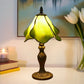 Tiffany table lamp with stained glass shade, glowing yellow-green tones, metal base
