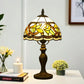 Tiffany-style table lamp with yellow stained glass shade and bronze metal base on table.