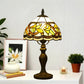 Tiffany-style stained glass table lamp with yellow shade and bronze metal base on sideboard.