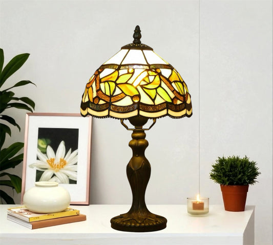 Tiffany-style stained glass table lamp with yellow shade and bronze metal base on sideboard.